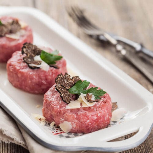 Carne cruda all’albese on a white serving dish with silverware and a grey napkin