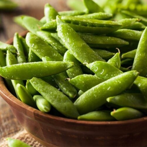 close up of snap peas in a wooden bowl