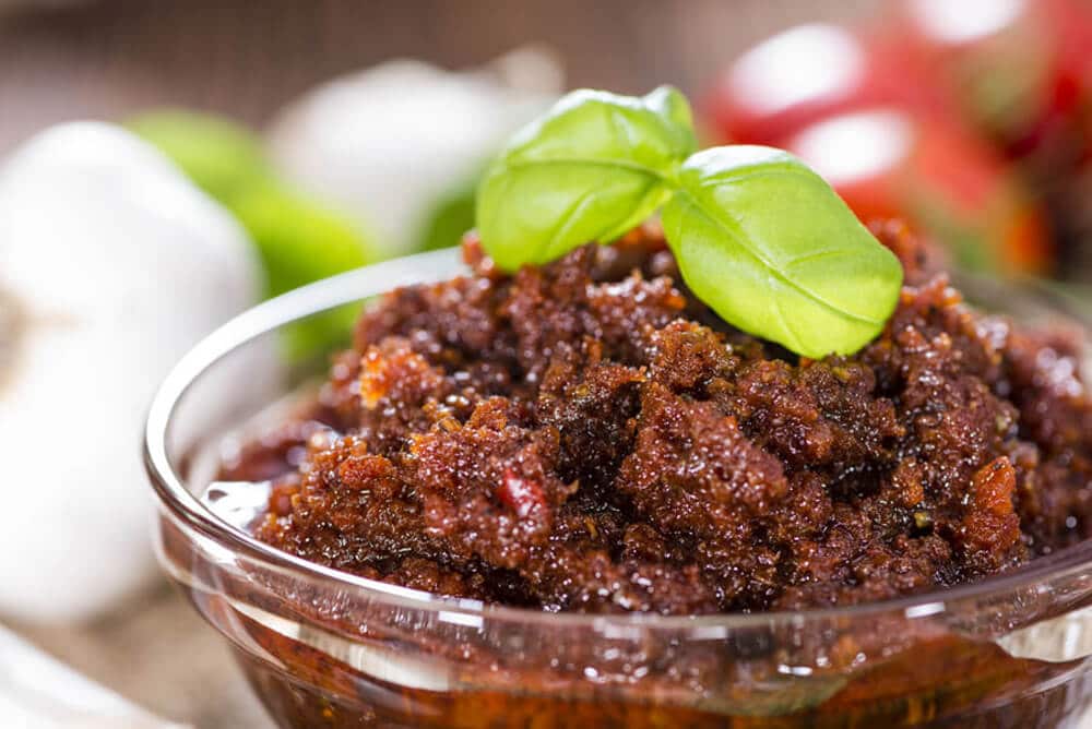 sun dried tomato pesto in a glass dish on a table, garnished with basil