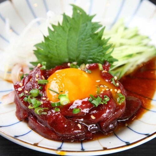 korean raw beef yukhoe on a plate with pear matchsticks and a shiso leaf.