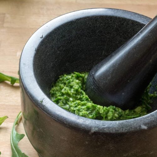 pesto in a black mortar and pestle with arugula leaves on the table