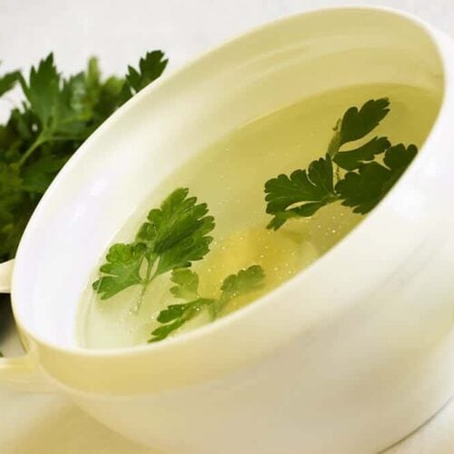 chicken broth in a white bowl garnished with parsley