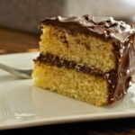 slice of gluten-free vanilla layer cake with vegan chocolate frosting on a white plate
