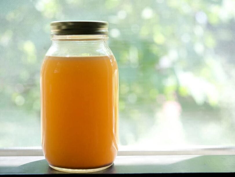 jar of crockpot chicken stock on a table by a window