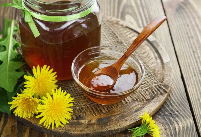 dandelion jelly in a bowl next to a jar and several dandelion blossoms