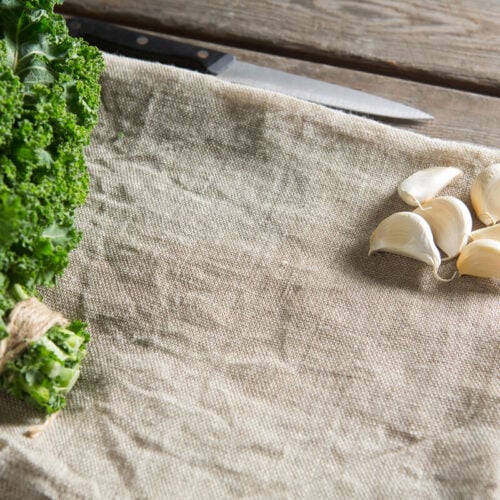 kale leaves and garlic cloves on a burlap napkin on a table