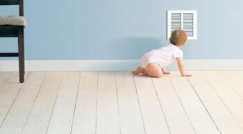 baby on a wood floor looking into an air vent