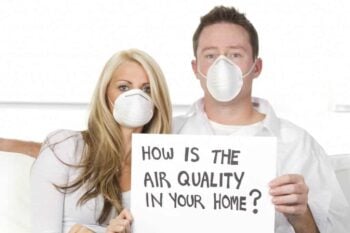 man and woman in facemasks holding a sign that says "How is the Air Quality in Your Home?"