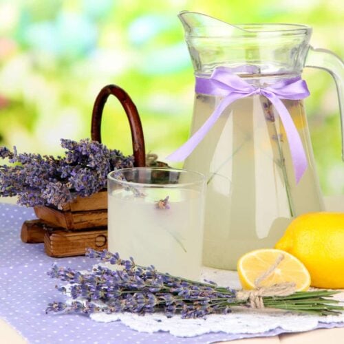 lavender lemonade in a pitcher on a table with lemons and lavender blossoms