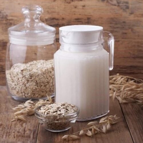 glass pitcher full of oat milk with bowl of oats on table