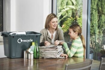 mother and child with a stack of newspapers and a recycling bin