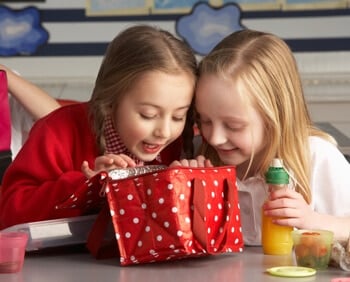 two girls looking into a red lunchbox with white polka dots.