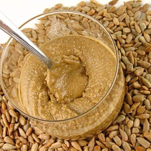 sunflower seed butter in a class bowl with a spoon on a bed of sunflower seeds