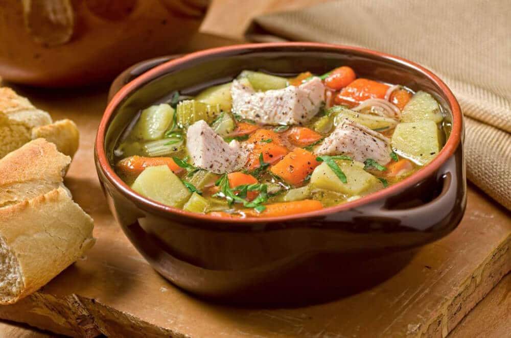 brown ceramic bowl full of turkey soup with root vegetables