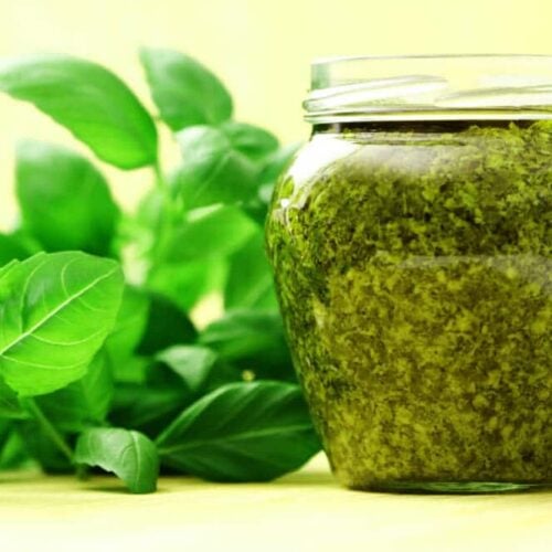 jar of pesto next to basil leaves