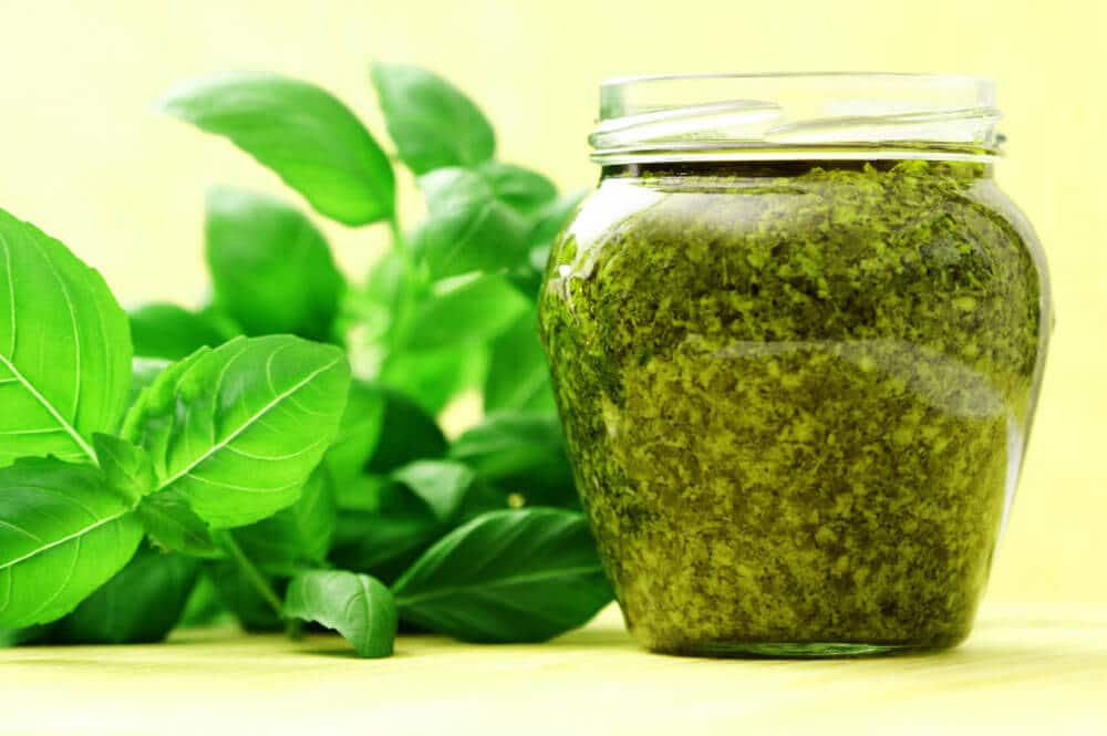 jar of pesto next to basil leaves