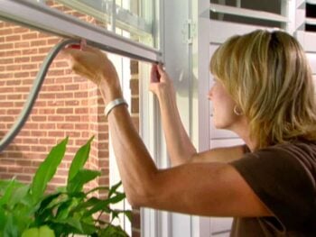 woman applying weatherstripping to a window.